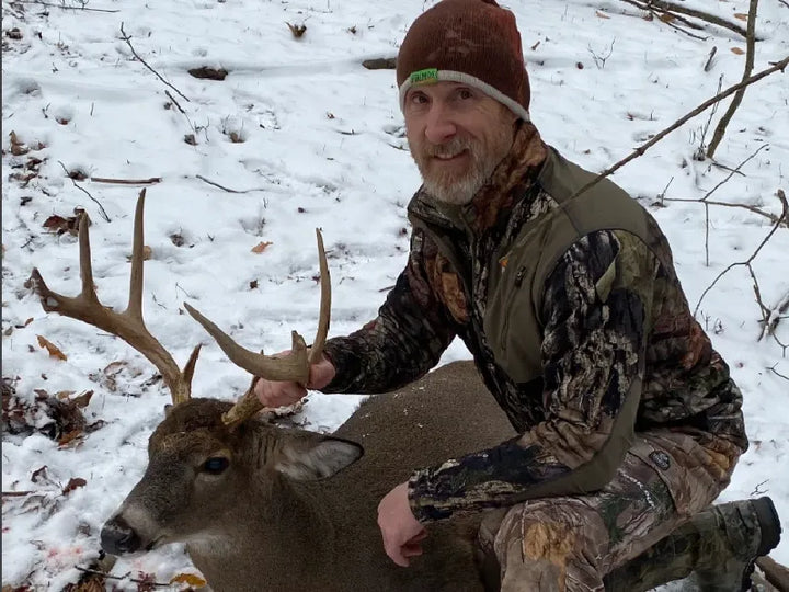 Hunter with a whitetail buck in a snowy forest, made possible by the GardePro X66 Pro's 7800mAh battery for all-season use